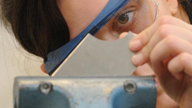 Eine Person mit Schutzbrille bearbeitet ein Werkstück mit einem Werkzeug.