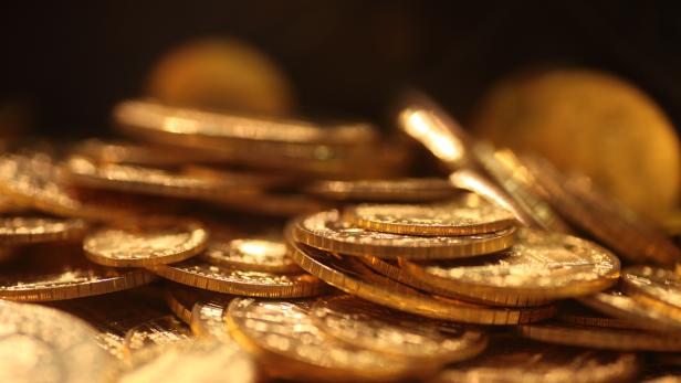 Viele goldene Münzen liegen übereinander gestapelt und glänzen im warmen Licht.