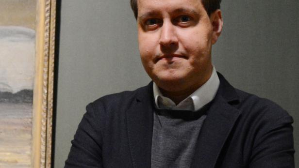 Ein Mann steht vor einem Gemälde mit verschränkten Armen.