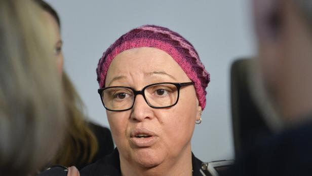 Eine Frau mit Brille und rosa Kopfbedeckung spricht.