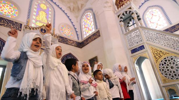Eine Gruppe Kinder singt in einer Moschee mit bunten Glasfenstern.