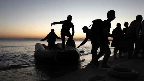 Menschen verlassen bei Sonnenaufgang ein Schlauchboot am Strand.