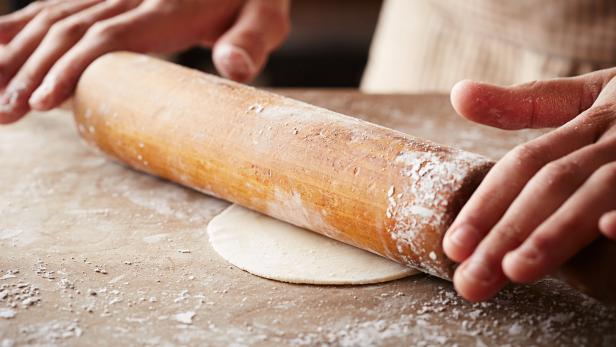 Ein Teig wird mit einem Nudelholz ausgerollt.