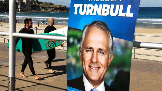 Zwei Surfer gehen am Strand entlang, im Vordergrund ein Wahlplakat von Malcolm Turnbull.