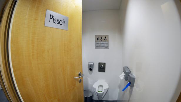 Ein Pissior mit einem Schild an der Tür, das darauf hinweist, dass nur Toilettenpapier in den Mülleimer gehört.