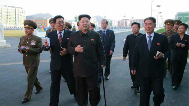 Kim Jong-un geht mit einer Gruppe von Militärangehörigen und Zivilisten eine Straße entlang.