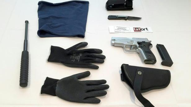 Auf einem Tisch liegen eine Pistole, ein Schlagstock, ein Messer, Handschuhe und eine Sturmhaube.