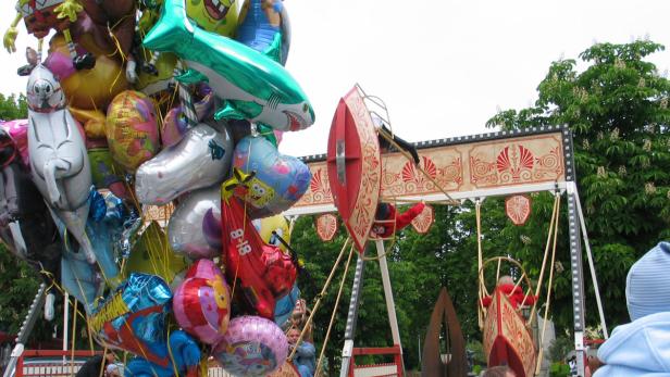 Ein bunter Ballonstand vor einem Karussell auf einem Jahrmarkt.