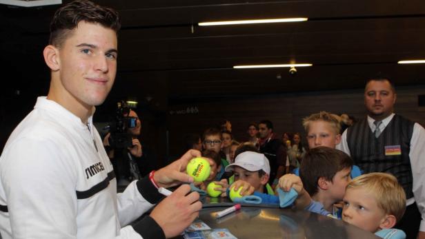Dominic Thiem gibt Autogramme auf Tennisbälle für eine Gruppe Kinder.