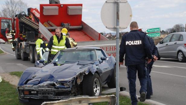 Ein beschädigter blauer Sportwagen nach einem Unfall, mit Feuerwehr und Polizei vor Ort.