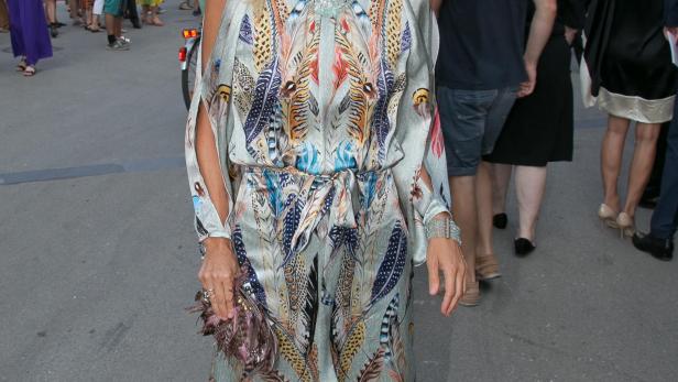 Eine Frau in einem langen, gemusterten Kleid steht in Salzburg vor der Festung Hohensalzburg.