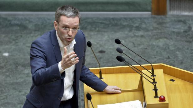 Ein Mann mit Brille gestikuliert an einem Rednerpult mit mehreren Mikrofonen.