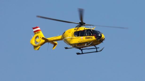 Ein gelber Rettungshubschrauber des ÖAMTC fliegt vor blauem Himmel.