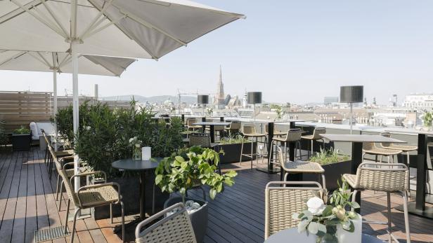 Eine Dachterrasse mit Tischen, Stühlen, Pflanzen und Blick auf Wien.