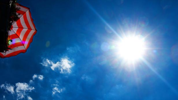 Ein rot-weiß gestreifter Sonnenschirm vor blauem Himmel und strahlender Sonne.