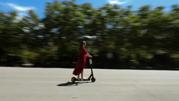 A woman rides an electric scooter through a road in Retiro Park in Madrid