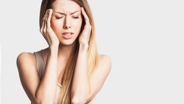 Eine Frau mit blonden Haaren hält sich die Schläfen und scheint Schmerzen zu haben.