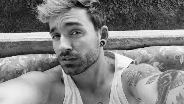 Ein Mann mit Tattoos und Ohrring blickt in die Kamera.