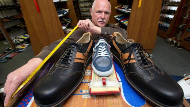 Ein Mann misst mit einem gelben Maßband die Länge von übergroßen Schuhen in einem Schuhgeschäft.