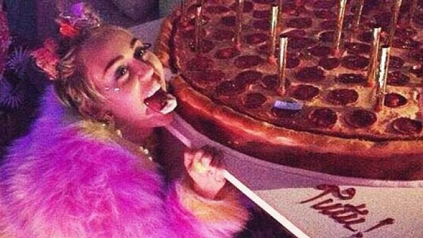 Miley Cyrus isst einen Marshmallow vor einer riesigen Pizza mit Kerzen zum Geburtstag.
