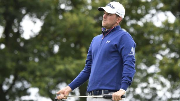 Ein Golfspieler mit blauem Pullover und weißer Kappe hält einen Golfschläger.