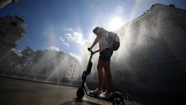 A man rides an electric scooter under water sprinklers during a heat wave in Vienna