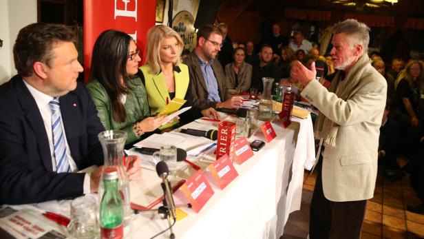 Eine Podiumsdiskussion mit mehreren Personen und einem Redner im Publikum.