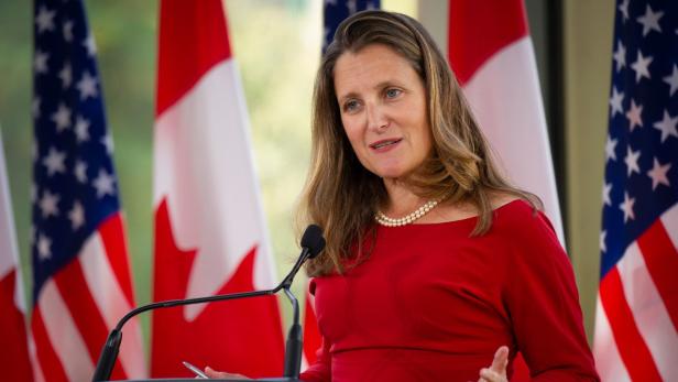 Chrystia Freeland spricht vor kanadischen und amerikanischen Flaggen.