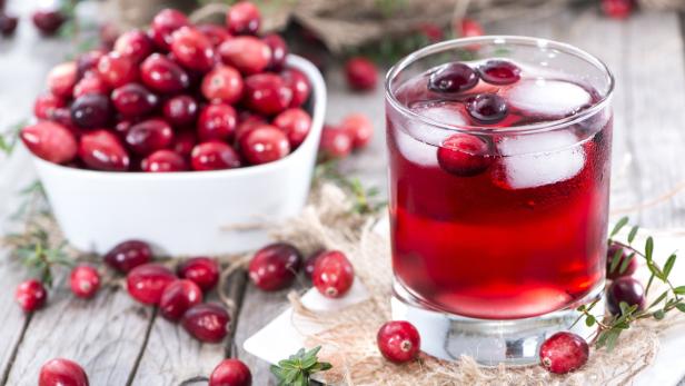 Ein Glas Cranberrysaft mit Eis, daneben eine Schüssel frischer Beeren