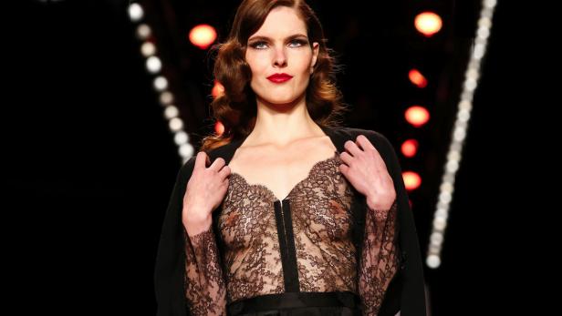 Eine Frau mit roten Lippen trägt ein durchsichtiges Spitzenoberteil auf dem Laufsteg.