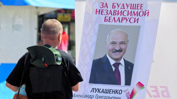 Ein Mann steht vor einem Wahlplakat von Alexander Lukaschenko.