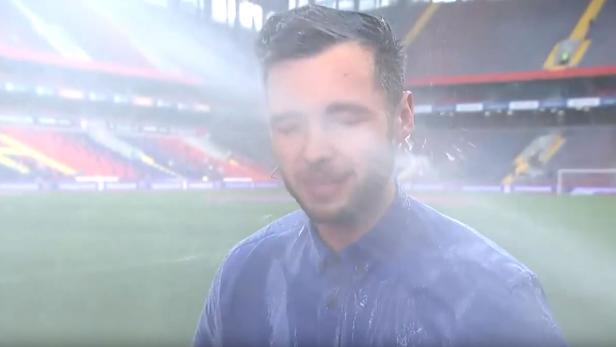 Ein Mann steht in einem Stadion und wird von Wasser bespritzt.