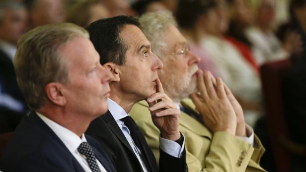 Drei Männer sitzen aufmerksam in einer Menschenmenge.