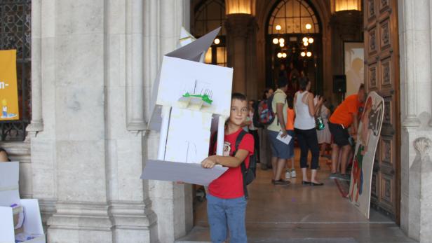 Xaver, an mehreren Tagen gewählter Kinderstadt-Politiker, trägt das Karton-Rathaus aus dem Rathaus