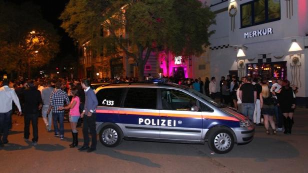 Ein Polizeiwagen steht vor dem Eingang des „Merkur“ Clubs, umgeben von einer Menschenmenge.