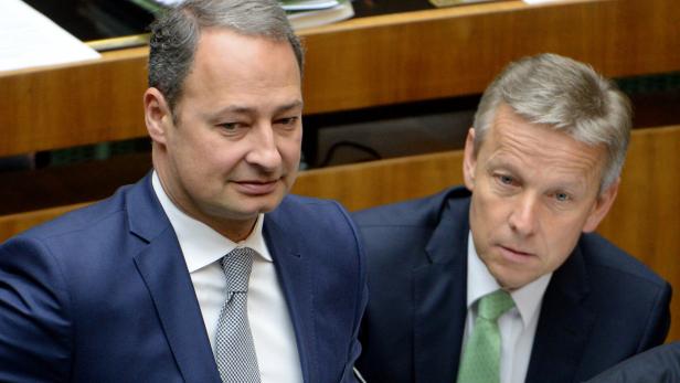 Zwei Männer in Anzügen sitzen nebeneinander.