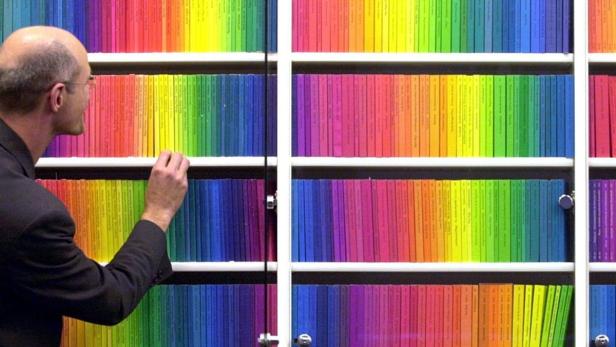 Ein Mann betrachtet ein Regal mit Büchern, die nach Farben sortiert sind.