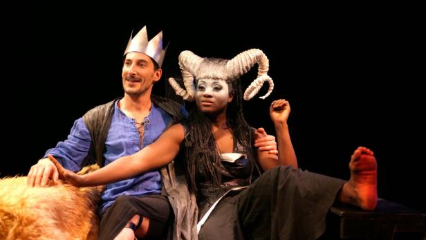 Ein Mann mit Krone und eine Frau mit Hörnern sitzen auf einer Bühne.