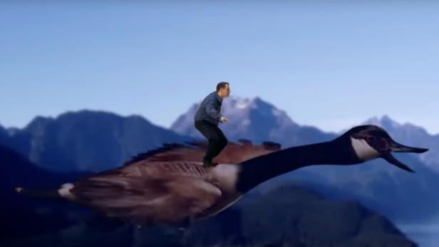 Ein Mann reitet auf einer fliegenden Gans vor einer Bergkulisse.