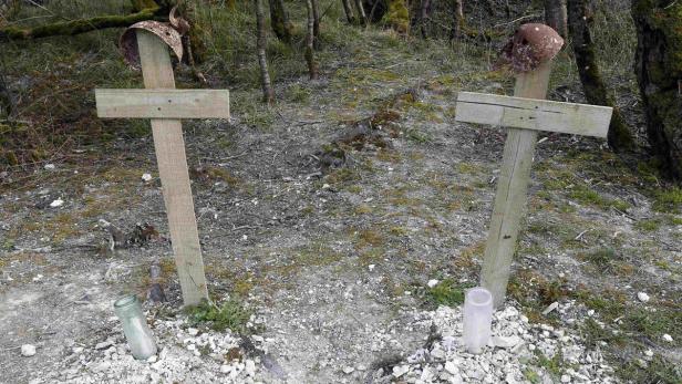 Zwei einfache Holzkreuze mit alten Helmen auf einem kleinen Friedhof.
