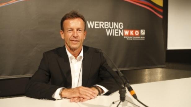 Ein Mann im Anzug sitzt an einem Tisch vor einem Werbebanner der Wirtschaftskammer Wien.
