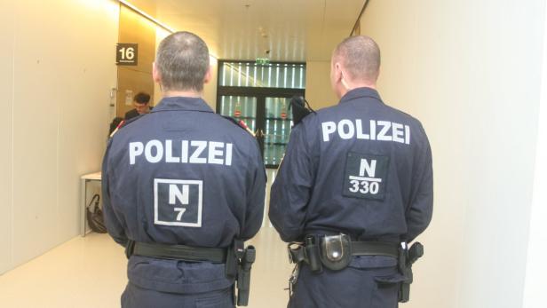 Zwei Polizisten stehen in einem hellen Flur mit dem Rücken zur Kamera.