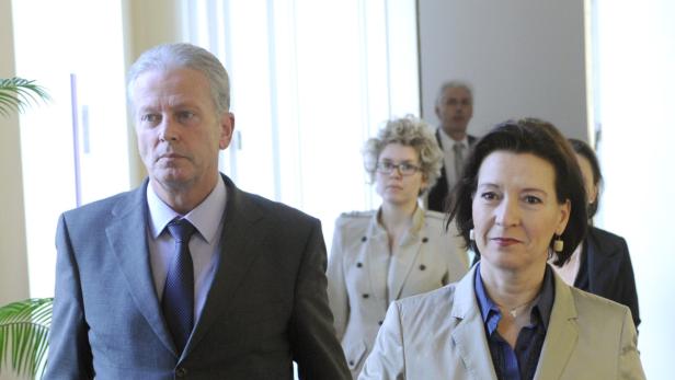 Eine Gruppe von Personen, darunter ein Mann im Anzug und eine Frau im Blazer, geht durch einen hellen Raum.