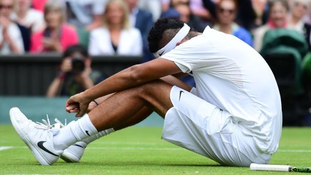 Ein Tennisspieler sitzt mit gesenktem Kopf und trauriger Haltung auf dem Rasen.