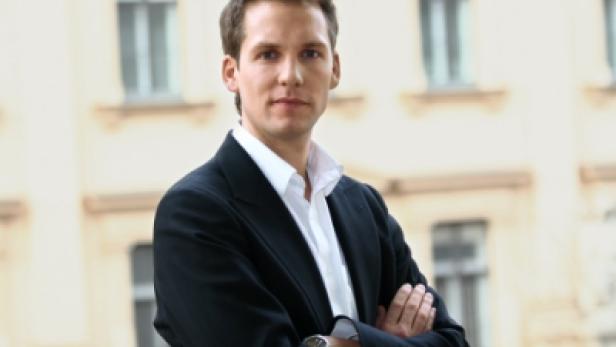 Ein Mann im Anzug steht mit verschränkten Armen vor einem Gebäude.