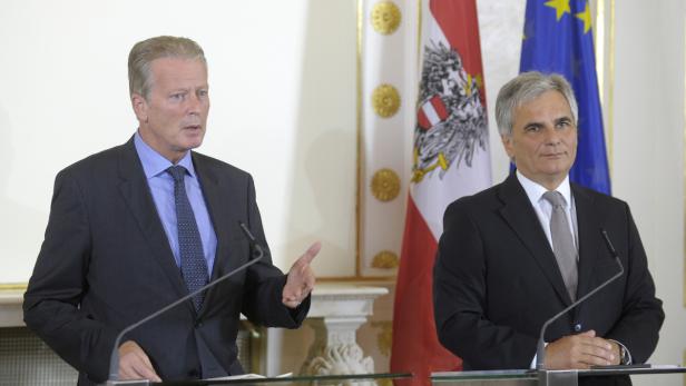 Zwei Männer in Anzügen stehen vor österreichischen und EU-Flaggen.