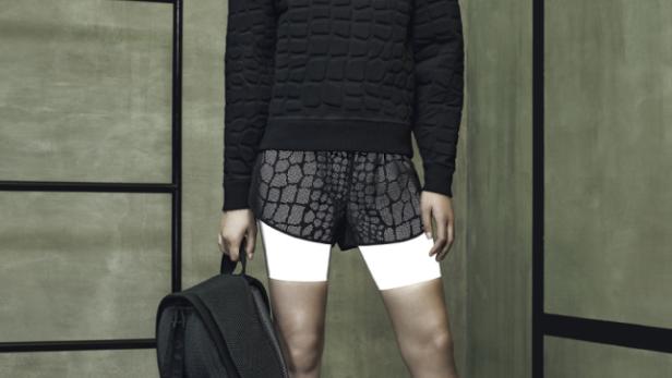 Eine Frau mit einer „WANG“-Mütze, einem schwarzen Trainingsanzug und Stiefeln posiert mit einem Rucksack.