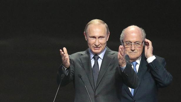 Wladimir Putin und Sepp Blatter gestikulieren vor einem dunklen Hintergrund.