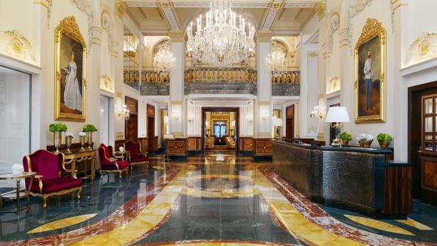 Die Lobby eines eleganten Hotels mit Marmorboden, Kronleuchtern und Porträtgemälden.