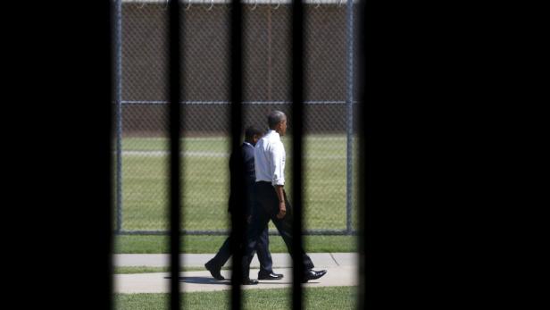 Barack Obama geht mit einer Begleitperson hinter einem Zaun entlang.